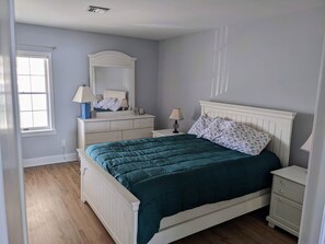Een slaapkamer met een bed, dressoir, nachtkastje en een raam.