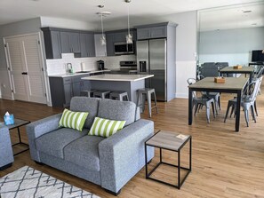A modern living space with a grey sofa, a dining table with chairs, a kitchen area with grey cabinets, and a small side table. - Stunning sunset and water views on Bay 2 bedrooms, 3 beds and 2 baths in OCNJ (Ocean City)