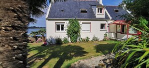 A two-story house with a sloped roof, a small garden, and a view of the sea. - Villa with sea view and private heated pool in the Crozon Peninsula (Finistère) (Landévennec)