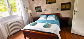 A bedroom with a wooden bed, a radiator, a window with curtains, and wall art. - Villa with sea view and private heated pool in the Crozon Peninsula (Finistère) (Landévennec)
