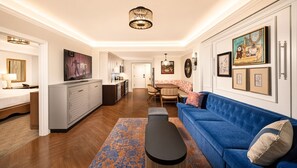 Una sala moderna con un sofá azul, una mesa de centro y un televisor. Hay una zona de cocina con armarios y una mesa de comedor.