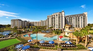 Un hotel con varias construcciones, una zona de piscina con sombrillas y un jardín ajardinado.