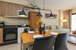 A modern kitchen with a dining area, equipped with a dishwasher, stove, and a dining table set for two. - Parque Albatross 5 - One Bed Apartment (Golf del Sur)