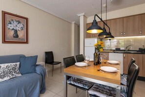 Un salon moderne avec une table à manger pour deux personnes, un canapé et un coin cuisine doté de meubles en bois et d’un four encastré.