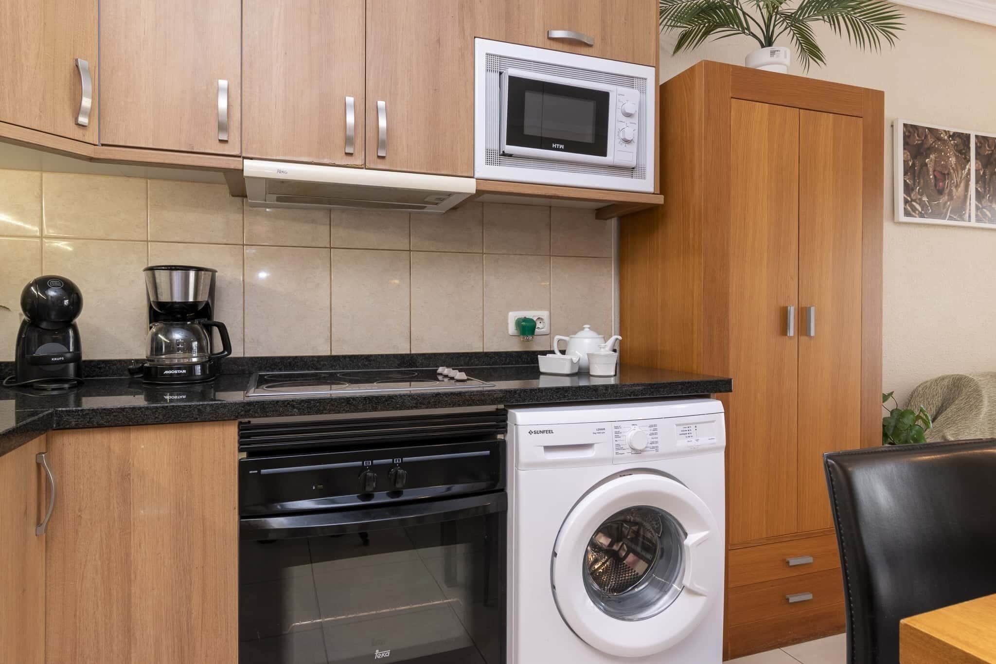 A compact kitchen with a microwave, stove, and washing machine.