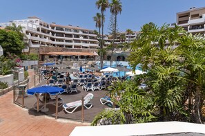 A resort pool area with sun loungers and umbrellas, surrounded by palm trees and hotel buildings. - Parque Albatross 5 - One Bed Apartment (Golf del Sur)