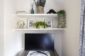 Un soggiorno con televisore a schermo piatto su un mobile, un camino e mensole con oggetti decorativi e piante.