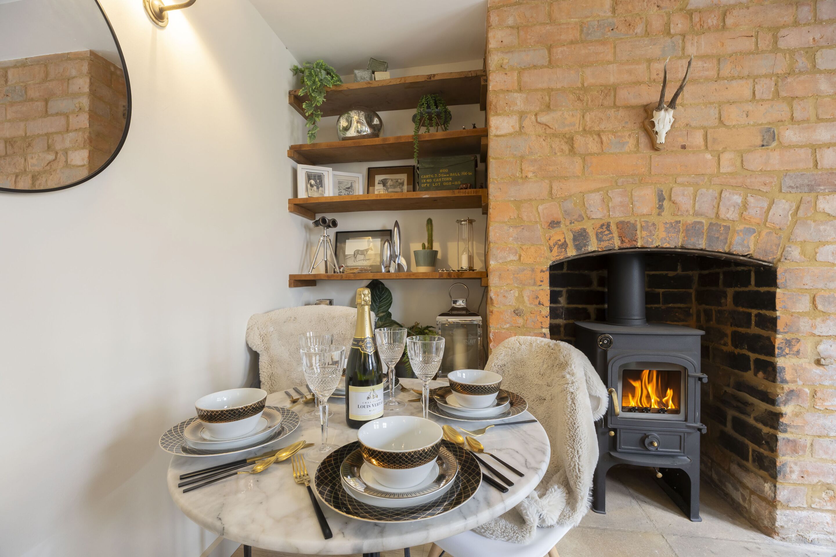 A dining area with a round table set for four, a fireplace, and shelves with decorative items.