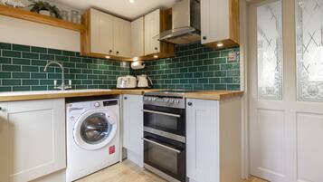 A compact kitchen with a washing machine, oven, and a green-tiled backsplash.