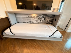 A bed with a white mattress and black trim, a wall-mounted TV, and a scenic mural above it. - Orlando | Family Riviera Retreat | Pool + Resort | 2BR (Lake Buena Vista)