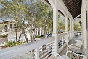 A covered outdoor area with white railings, a table with chairs, and a view of a residential street with trees and parked cars. - Carriage House with Gulf Views (Rosemary Beach)