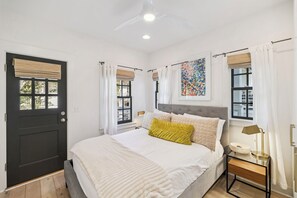 A bedroom with a bed, bedside tables, a window with curtains, a ceiling light, and a wall-mounted artwork. - Carriage House with Gulf Views (Rosemary Beach)