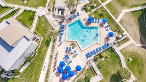 An aerial view of a resort with a central swimming pool, multiple lounge areas, and surrounding greenery.