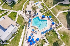 An aerial view of a resort with a central swimming pool, multiple lounge areas, and surrounding greenery.
