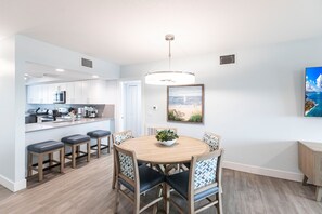 A modern kitchen with white cabinets and stainless steel appliances, a dining area with a wooden table and chairs, and a large window with a view of the ocean. - Sanibel Beach Club  (Sanibel)