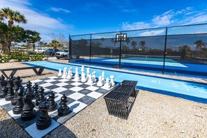 A checkered chessboard with pieces set up, a pool area with a fence, and a clear sky. - Sanibel Beach Club (Sanibel)