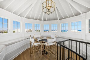 A spacious room with a high ceiling, large windows, a central seating area with a table, and a view of the sea. - Porches | Gulf Views | Carriage House (Rosemary Beach)