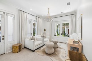 A modern living room with a white sofa, ottomans, a wooden coffee table, and a chandelier. - Porches | Gulf Views | Carriage House (Rosemary Beach)