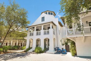 A white two-story building with a balcony, arched doorways, and a bicycle parked in front. - Porches | Gulf Views | Carriage House (Rosemary Beach)