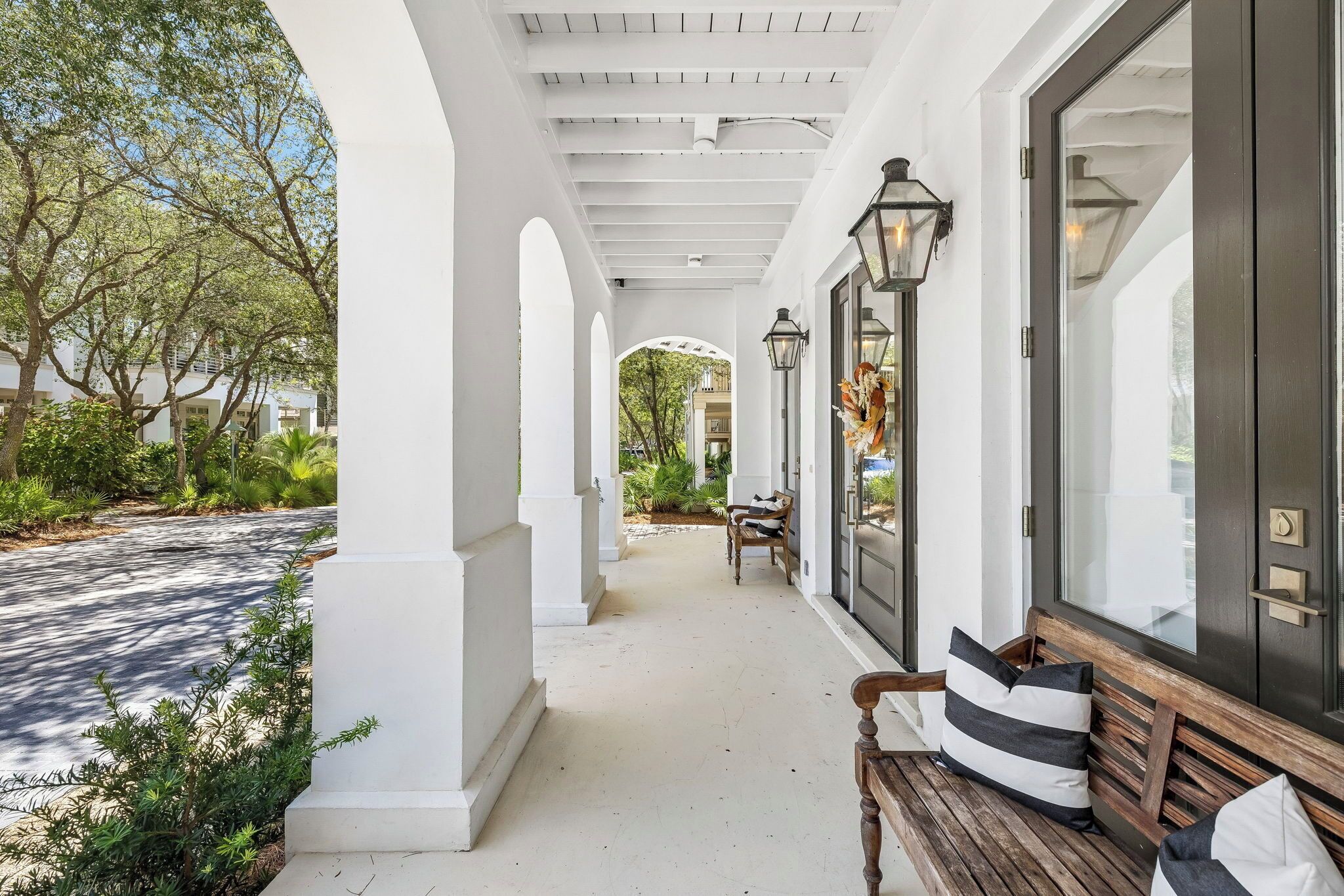 A covered porch with a bench, a door with a decorative wreath, and a view of a garden.