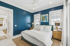 A bedroom with a bed, a nightstand, a lamp, and a painting on the wall. - Porches | Gulf Views | Carriage House (Rosemary Beach)