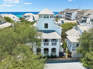 A coastal residential area with multiple houses, a prominent central building with a gabled roof, and a clear view of the ocean. - Porches | Gulf Views | Carriage House (Rosemary Beach)