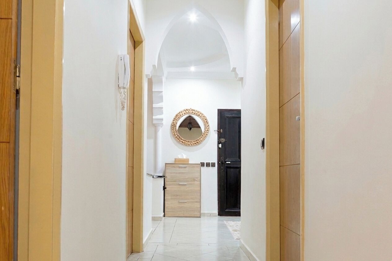 Un pasillo con una puerta de madera, una puerta negra y un espejo fijado a la pared.