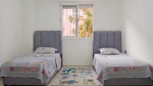 Un dormitorio con dos camas individuales, una ventana con vistas a palmeras y una alfombra estampada en el suelo.