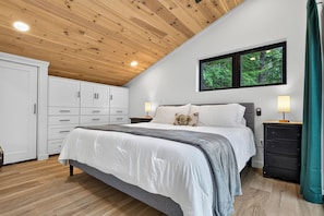 A bedroom with a bed, nightstands, a wardrobe, and a window with a view of trees.
