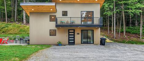 Ein modernes, zweistöckiges Gebäude mit Balkon, Tür und kleinem Garten.