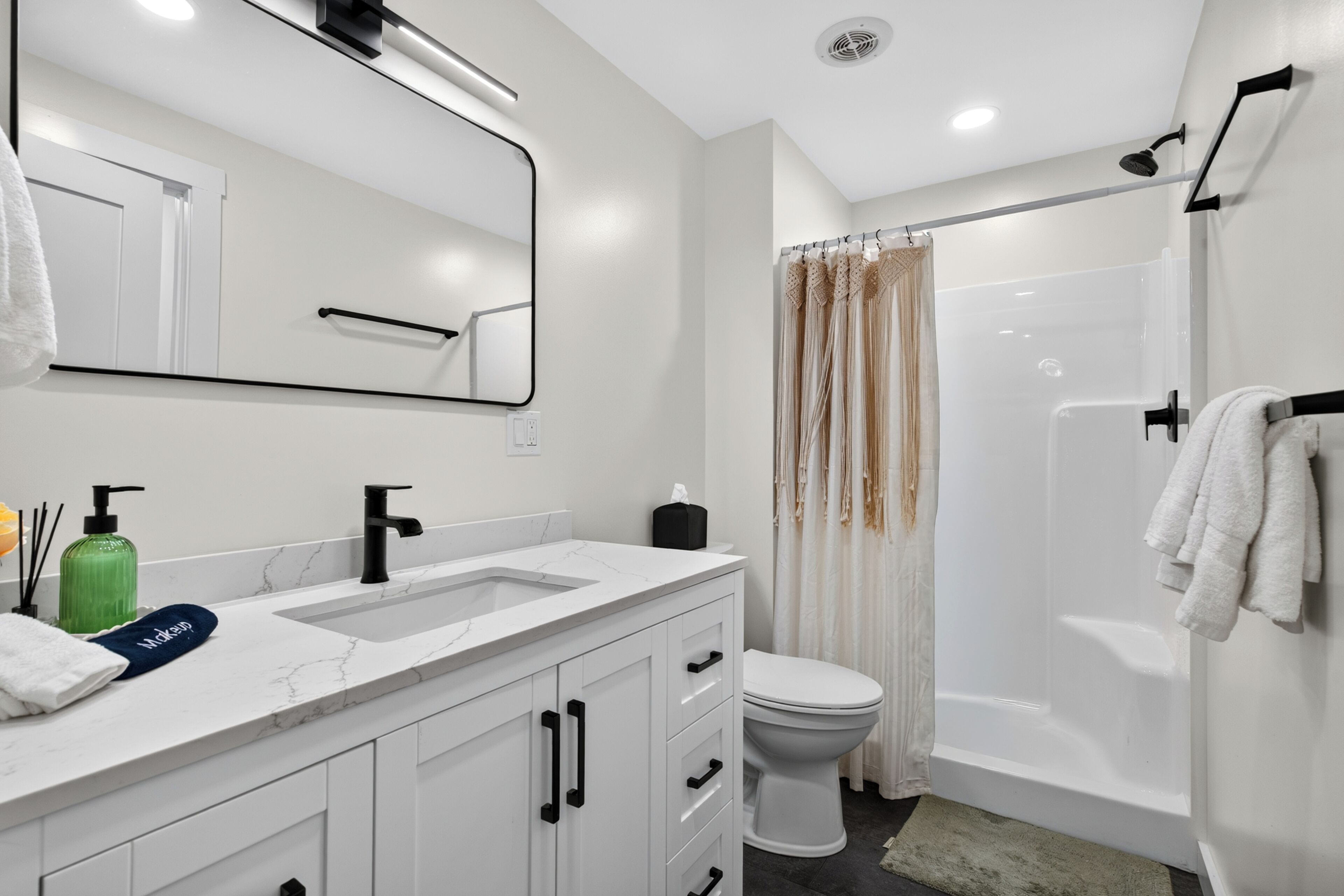 A modern bathroom with a white sink, black faucet, and a toilet. There is a shower area with a glass door and a towel rack with white towels.