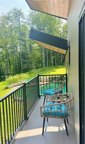 A balcony with wicker chairs and cushions, a view of a green landscape, and a wooden ceiling.