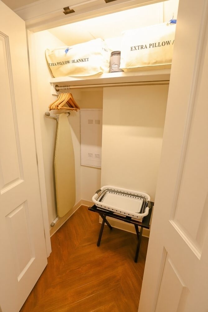 A narrow hallway with a wooden floor, a white door, and a small ironing station with an ironing board and a hanging garment.
