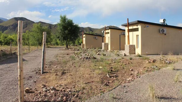 A rural property with two single-story buildings, a dirt road, and a mountainous backdrop.