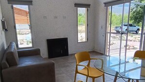 A spacious living room with a sofa, two yellow chairs, a glass table, and a fireplace.