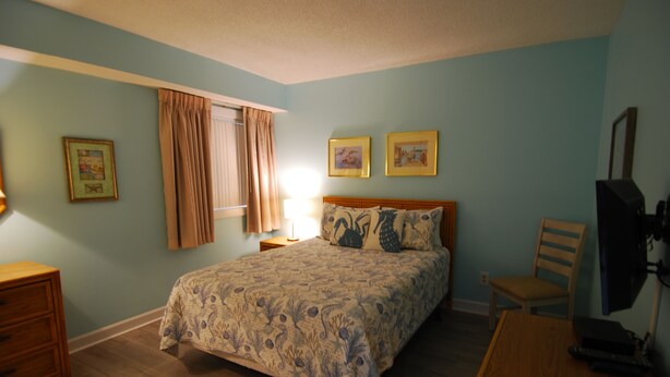 A bedroom with a bed, a desk, a chair, a window with curtains, and two framed pictures on the wall. - 3BR Oceanfront Condo at Land's End! (Myrtle Beach)