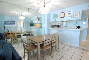 A dining area with a wooden table and chairs, a kitchen with a microwave and refrigerator, and a living room with a couch and a TV. - 3BR Oceanfront Condo at Land's End! (Myrtle Beach)