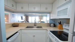 A modern kitchen with white cabinets, a stainless steel sink, a toaster, and a stove. - 3BR Oceanfront Condo at Land's End! (Myrtle Beach)
