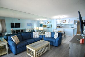 Ein modernes Wohnzimmer mit einem blauen Sofagarnitur, einem Holztisch und einer Küchenzeile mit Esstisch.