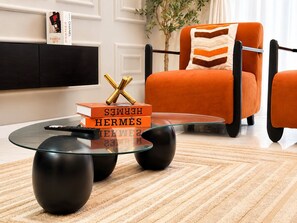 A modern living room with a glass coffee table, a black sofa, and a bookshelf.