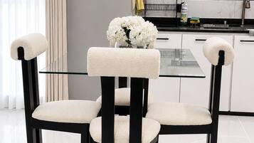A modern dining area with a glass-top table and four chairs with cushioned seats and backs.