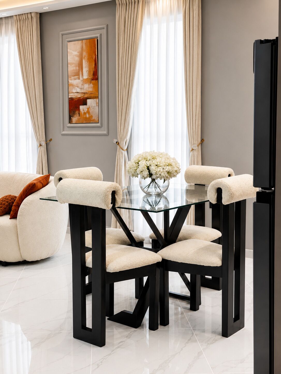 A modern dining area with a glass table surrounded by chairs, a sofa, and a vase of flowers.