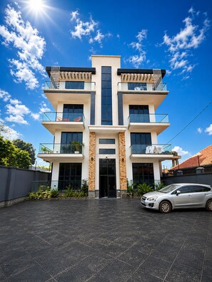 A multi-story building with a central entrance, balconies on each floor, and a car parked in front.