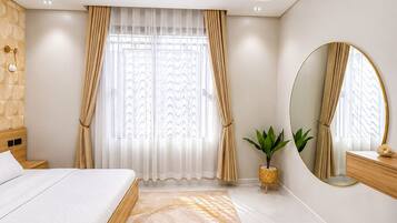A modern bedroom with a large bed, a round mirror, a potted plant, and a wooden nightstand.