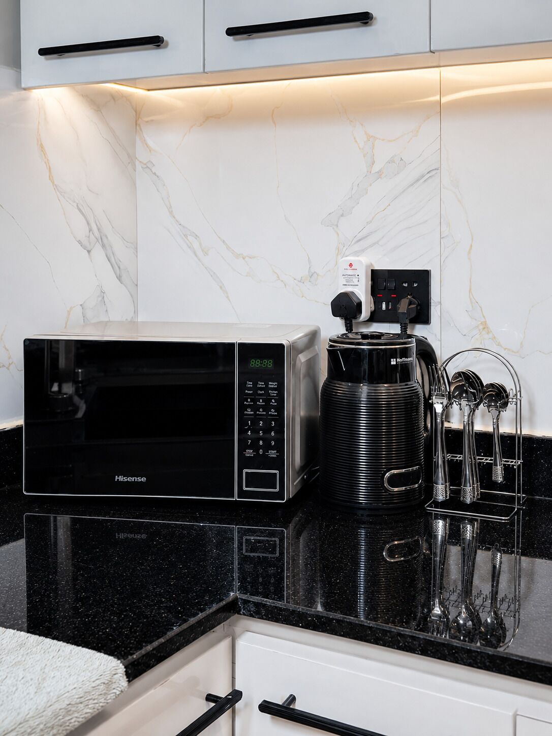 A kitchen with a black Hisense microwave, a coffee maker, and a utensil holder on a black countertop.