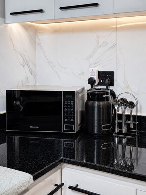 Una cocina con un microondas Hisense negro, una cafetera y un organizador de utensilios sobre una encimera negra.