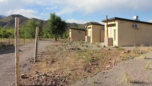 A rural property with two single-story buildings, a dirt road, and a mountainous backdrop.