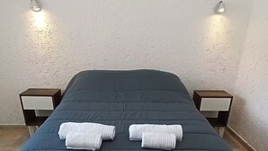 A bed with a dark blue duvet, two white towels, and two bedside tables with wall-mounted lamps.