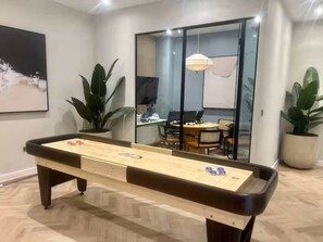 Ein Billardtisch in einem modernen Raum mit einer Glaskabine, Zimmerpflanzen und einem Essbereich im Hintergrund.