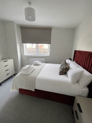 Ein Schlafzimmer mit Bett, Nachttisch, Kommode, einem Fenster mit Blick und einer Deckenleuchte.